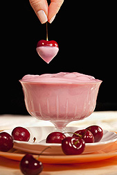 Photo: A small glass ramekin containing cherry yogurt and a hand dangling a fresh cherry above it. Link to photo information