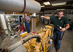 Agricultural engineer and technician prepare a microturbine for operation with a wind-hybrid system while another agricultural engineer measures emissions from a diesel generator: Click here for full photo caption.