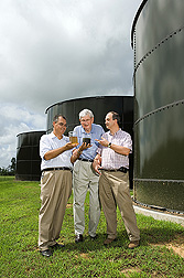ARS soil scientists and the CEO of Terra Blue, Inc., examine swine wastewater before (dark liquid) and after (clear liquid) treatment in the second-generation system they invented: Click here for full photo caption.