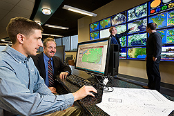 ARS hydrologist (far left) and Penn State University climatologist examine regional data they are using to develop a Web-based “fertilizer forecast." The program will use a range of weather variables, including the type of meteorological data Penn State associate professor and ARS soil scientist (far right) are studying in the background: Click here for full photo caption.