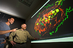Molecular biologist (left) and computational biologist examine a molecular model of a protein involved in iron uptake by bacteria: Click here for full photo caption.