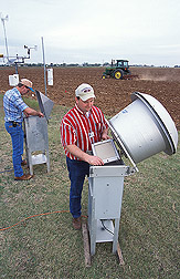 Agricultural engineer (left) and former ARS scientist, now with Oklahoma State University, Stillwater, change filters from particulate-matter samplers and collect meteorology data while sampling dust generated by a rolling cultivator (background): Click here for full photo caption.