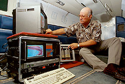 Aboard an aircraft, a remot-sensing specialist adjusts a three-camera, multispectral video system. Click here for full photo caption.