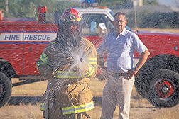 Northwest Fire District Captain uses water and chemical wetting agent to subdue Africanized honey bees while entomologist looks on: Click here for full photo caption.