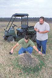 Technician measures a black imported fire ant mound while an entomologist records data: Click here for full photo caption.