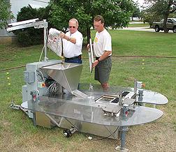 Entomologist (left) and technician load corn, used as bait to attract deer, into the hopper of an automatic deer-collaring device: Click here for full photo caption.