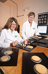 Research assistant Sharon Croskey (left) of Ohio State University cuts whole-grain wheat flour cookie dough for baking-quality tests as ARS technician Amy Bugaj sets baked cookies on a cooling rack: Click here for photo caption.