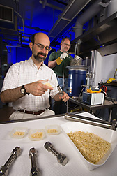 Biochemical engineer (left) loads reactor vessels with corn fiber while microbiologist lowers samples into a sand bath heater to pretreat for fermentation: Click here for full photo caption.