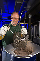 Microbiologist lowers vessels containing corn fiber into a sand bath heater to pretreat for fermentation: Click here for full photo caption.