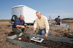 Agricultural engineer Bryan Woodbury (front left) collects a soil sample to characterize soil conditions following the field application of beef manure while agricultural engineer John Gilley (front right) and biological sciences aides adjust small wind tunnel equipment to be used for air quality measurements.