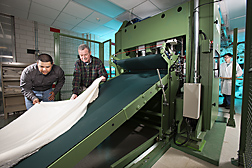Technician (left) and textile chemist (center) examine a cross-lapped web (batt) as they prepare to feed it into the needle-punch machine to produce a fabric containing mostly cotton. Another technician waits for the fabric on the exit side: Click here for full photo caption.