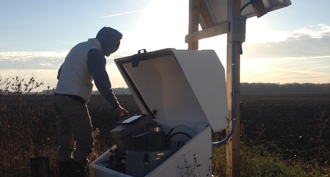 A photo of a scientist collecting data from equipment in the field at sun rise.