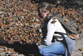 Woman with backpack surrounded by and covered with Monarch butterflies