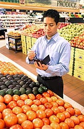 Photo: Man in a grocery store produce aisle checking information on a hand held device. Link to photo information