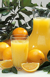 Photo: A pitcher and glass of fresh squeezed orange juice beside some fresh oranges.