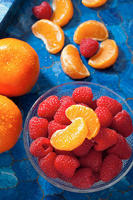 Red raspberries and mandarin oranges on a blue tray