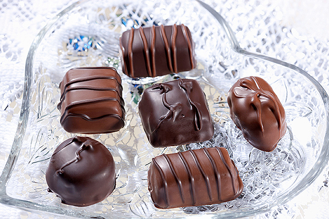 Six pieces of chocolate candy in a heart shaped glass dish.