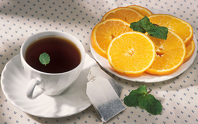 A cup of hot tea and a plate of orange slices and mint.
