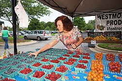 A woman selects a quart of blueberries at a farmers market.