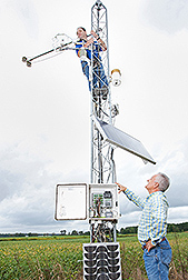 Two scientists working with a meteorological tower in a field