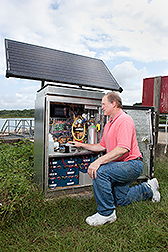 A scientist kneeling beside sensing equipment in a field 