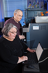 Two scientists using a mass spectrometer and looking at data on a screen