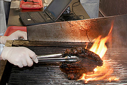 Photo: A sirloin steak is being turned over on a flaming grill. Link to photo information