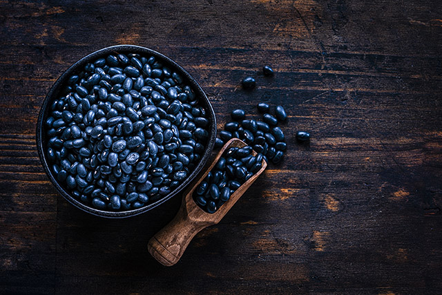 Black beans in a bowl on a wooden table with a serving scoop of beans beside the bowl. 